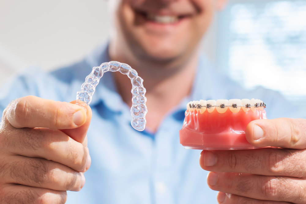 Invisalign Clear Aligners Treatment Option Hands holding a clear aligner and dental model showing orthodontic treatment choices