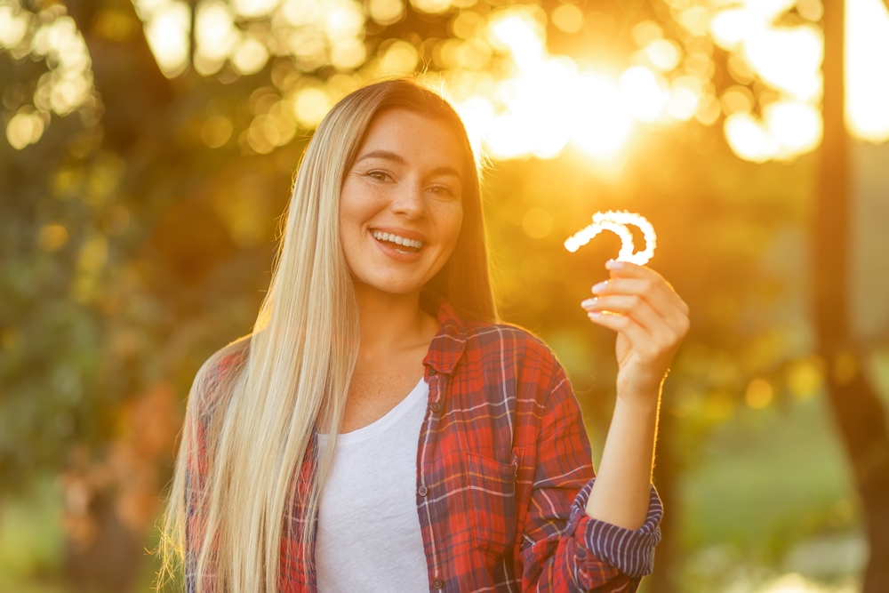 Invisalign Smile Transformation Journey – Invisalign Irvine A smiling patient holding clear aligners during golden-hour lighting for orthodontic care – Invisalign Irvine