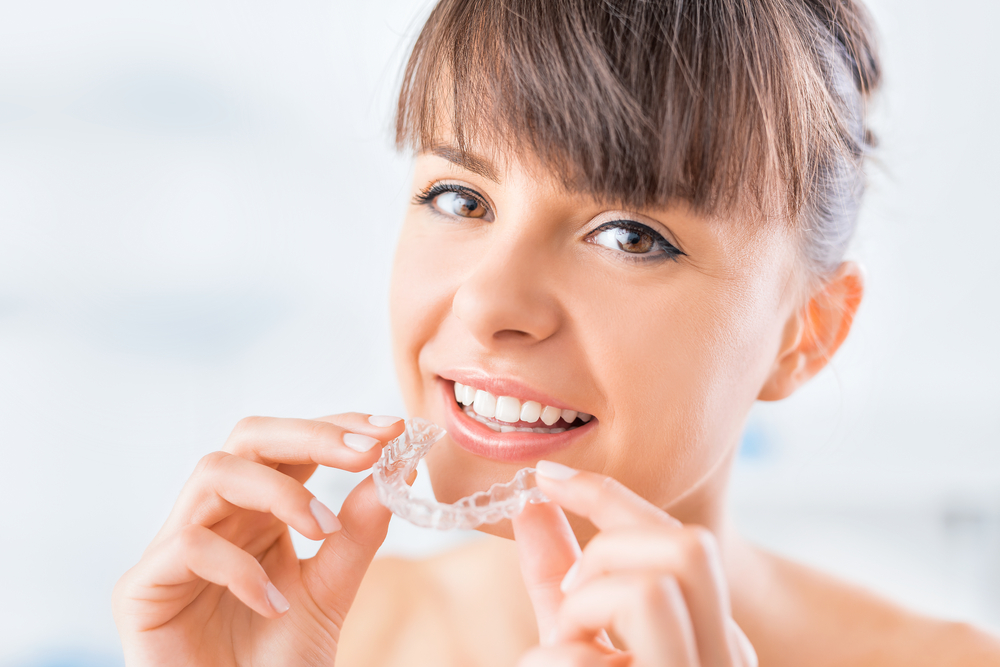A close-up of a woman holding a clear dental aligner to support orthodontic treatment – Invisalign Irvine