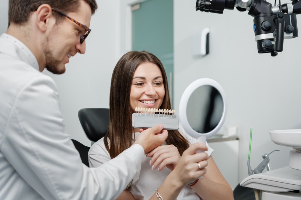 Cosmetic Veneer Shade Consultation A dentist helps a smiling patient choose the perfect tooth shade